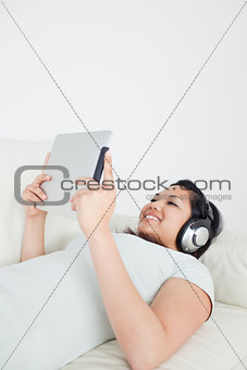Woman lying on a sofa with headphones on and holding a tactile t
