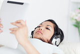 Woman lies on a coach and holds a tactile tablet with headphones