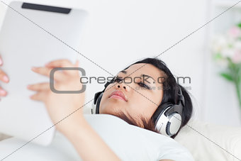 Woman lies on a coach and holds a tactile tablet with headphones
