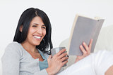 Woman smiling while holding a grey mug and a book