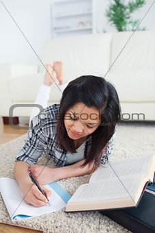 Woman writing on a notebook while lying on the floor