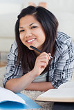 Smiling woman holding a pen as she lays on the floor
