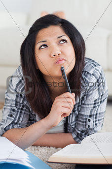 Thinking woman laying on the floor while holding a pen with a bo