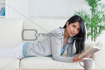 Woman laying on a sofa while reading a book