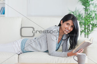 Smiling woman laying on a sofa while reading a book