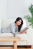 Woman reading a book with a mug on a table while resting on a co