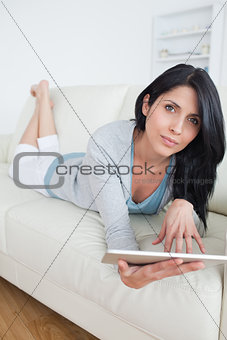Woman lying on a sofa while playing with a tablet
