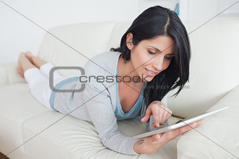 Woman laying on a sofa while holding a tablet