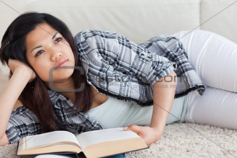 Thinking woman lying on the floor while holding a book