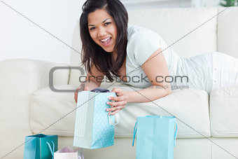 Woman holding up a shopping bag while lying on a sofa