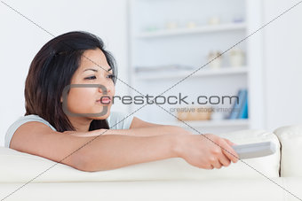 Woman pressing on a television remote while sitting on a white c