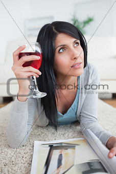 Woman thinking while holding a glass of red wine and a magazine