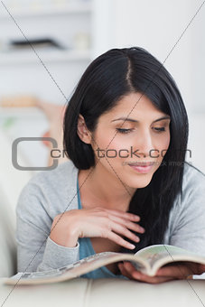 Woman reading a book while lying on a couch and touches her hair