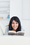 Woman holding a book while smiling and lying on a couch