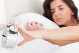 Brunette woman trying to turn off her alarm clock