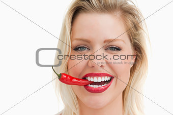 Happy woman biting a red chili while standing