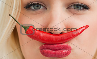 Young woman placing a chili between her nose and her mouth