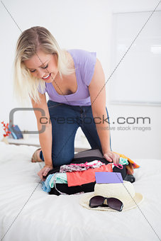 Young woman trying to close her luggage