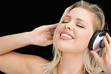 Joyful blonde woman listening to music through headphones