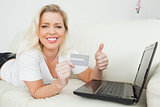 Woman with a thumb up and a credit card using a laptop