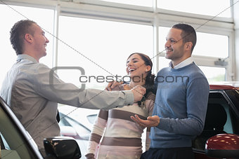 Laughing couple receiving keys from a salesman