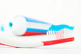 Tube of toothpaste next to a red toothbrush