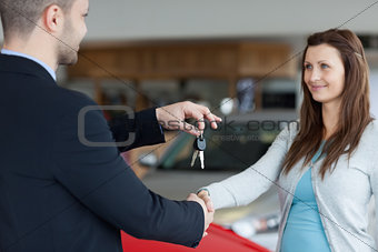 Salesman giving car keys while shaking hand of a woman