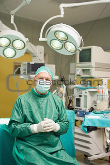 Smiling surgeon sitting while joining his hands together