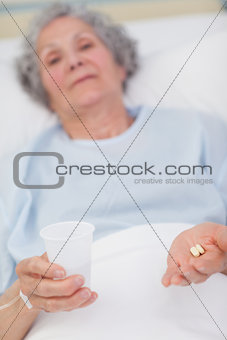 Patient holding drugs and plastic glass in her hands