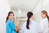 Nurse smiling while standing in a hallway with a patient and a d