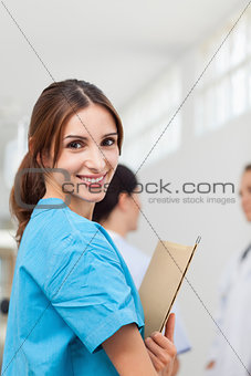 Nurse smiling while holding files and standing with a doctor and