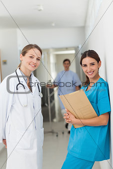 Doctor and a nurse against a wall standing side by side in a hal