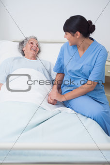 Nurse sitting on the medical bed next to a patient