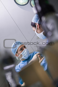 Serious doctor giving a surgical scissor to a nurse
