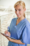 Nurse looking at camera while writing on a clipboard 