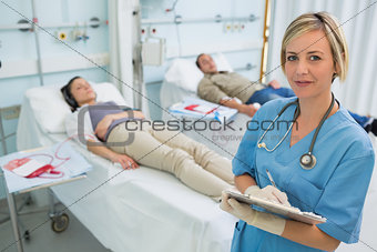 Nurse next to transfused patients writing on a clipboard