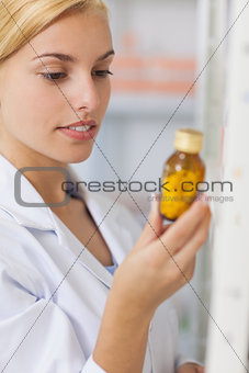 Blonde pharmacist looking at a drug bottle