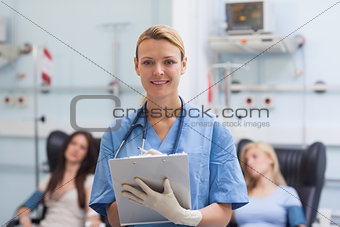 Nurse writing on a clipboard next to patients
