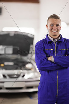 Smiling mechanicarms crossed next to a car