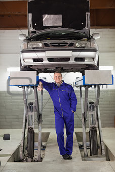 Smiling mechanic standing below a car
