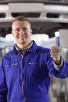 Mechanic standing with thumb up next to a car
