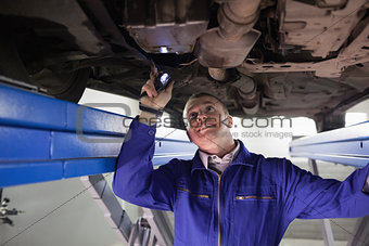 Smiling mechanic illuminating a car with a flashlight