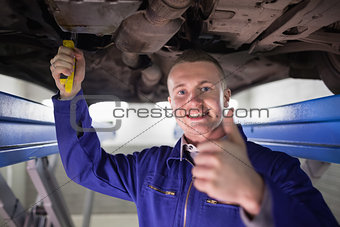 Smiling man repairing a car with his thumb up
