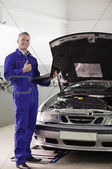 Smiling mechanic holding a computer with thumb up