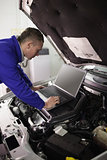 Mechanic looking at a computer on a car engine