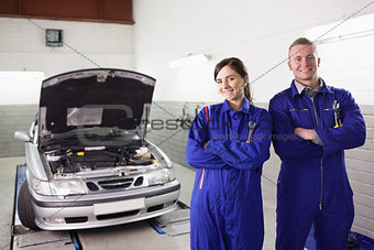 Smiling mechanics with arms crossed next to a car