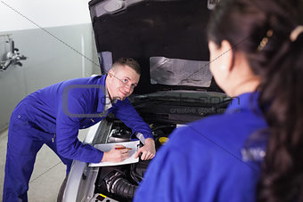 Mechanic leaning on a car looking at a colleague