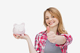Woman holding a piggy bank with her thumb up