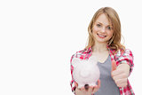 Woman with thumb up while holding a piggy bank