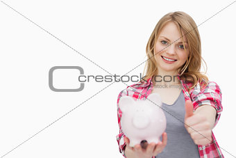 Woman with thumb up while holding a piggy bank